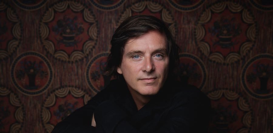 Mann med mørkt hår, mørk genser på mørk bakgrunn.