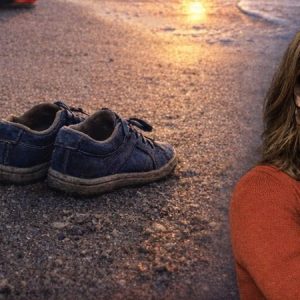 Kvinne med raude klede. Bakgrunn er ei strand med sko som står att