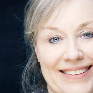 Portrett av kvinne med lyst hår mot mørk bakgrunn