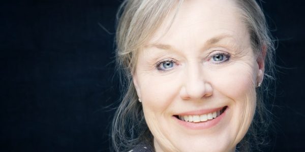 Portrett av kvinne med lyst hår mot mørk bakgrunn