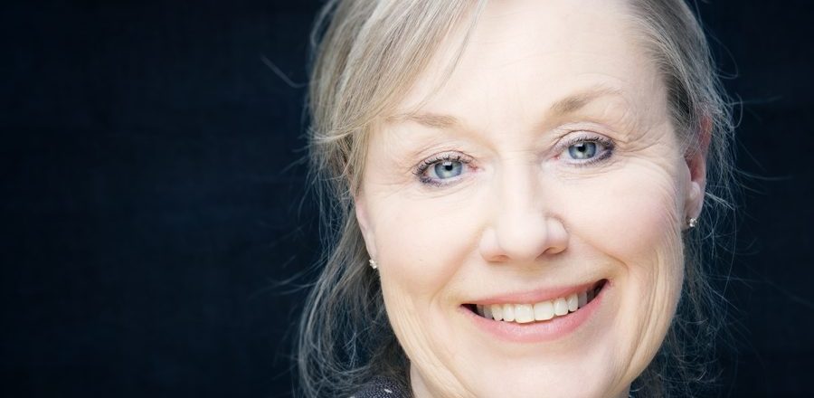 Portrett av kvinne med lyst hår mot mørk bakgrunn