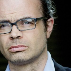 Mann med blå skjorte, briller og mørk dress