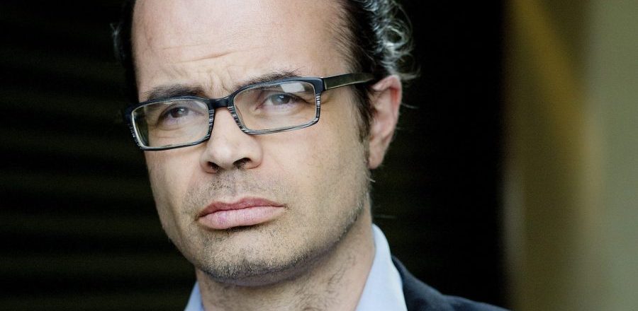 Mann med blå skjorte, briller og mørk dress